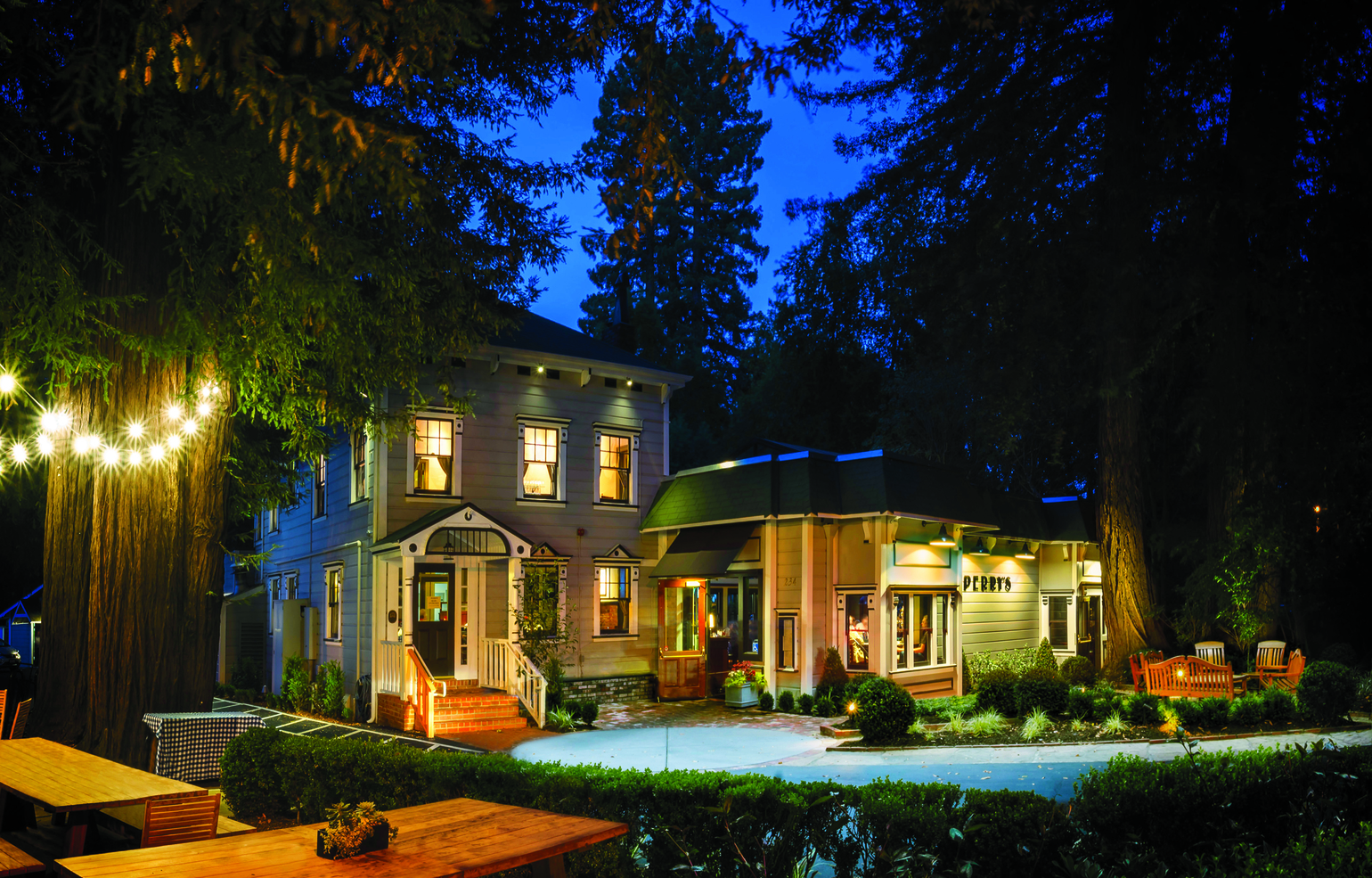A brightly lit house at night, featuring a cozy patio and surrounding trees, creating a warm and inviting atmosphere.