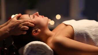 Woman lay on couch on her back with closed eyes and enjoy. Man make relaxing and therapeutic head massage at weight. Spa client has thrown her head back and rejuvenate. Wellness procedures in spa salon concept.