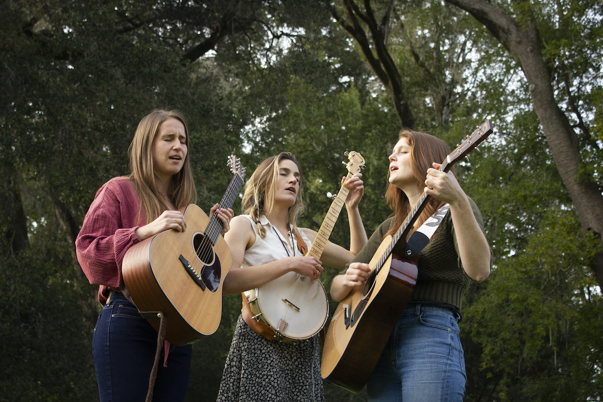 Musicians of Wyld Iris sing in the woods with guitars and banjo.