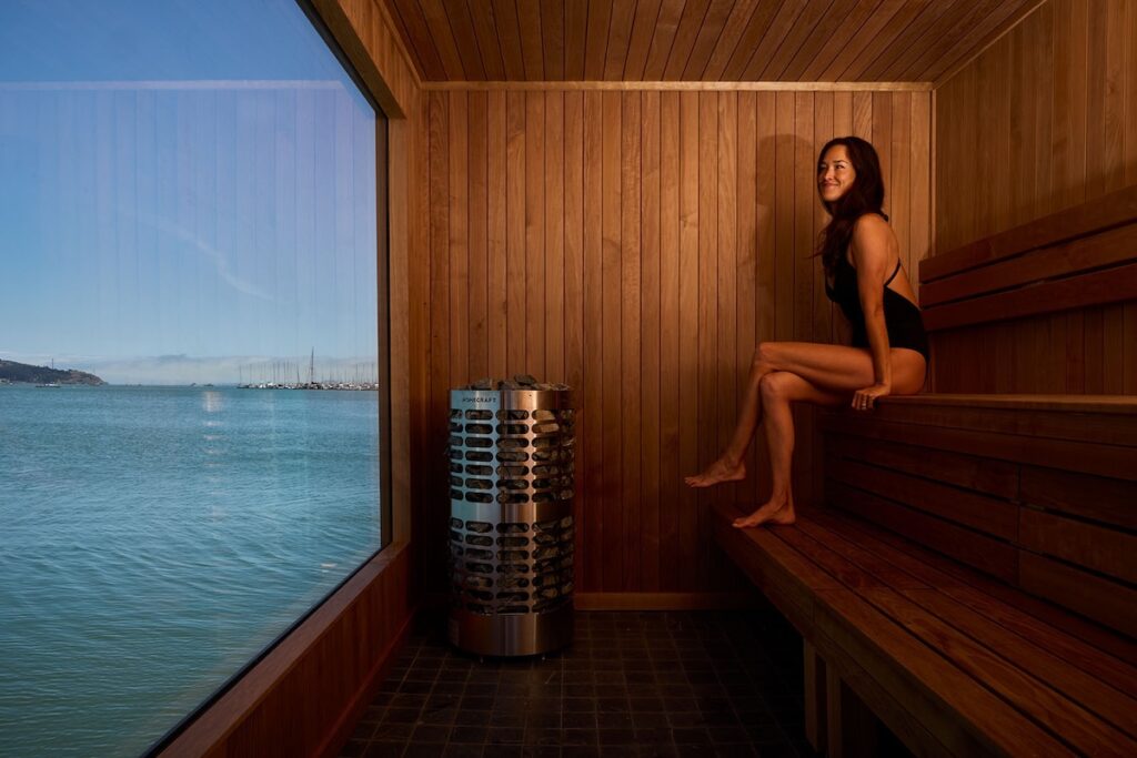 A woman sitting in a sauna overlooking the bay.