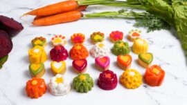 A white marble countertop with colorful gourmet dog treats and a bunch of carrots.