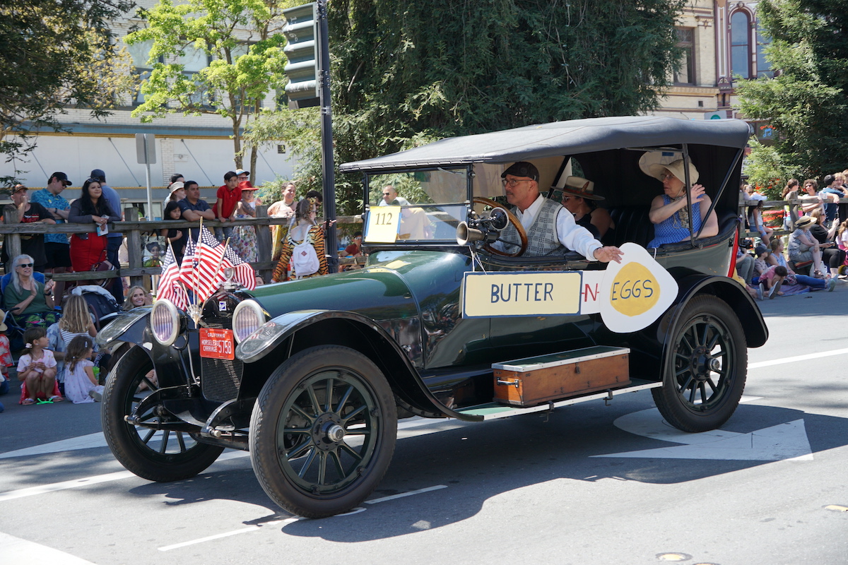A man waves from a green vintage car, with a sign saying "Butter and Eggs" for Petaluma's annual Butter and Eggs Day Parade 