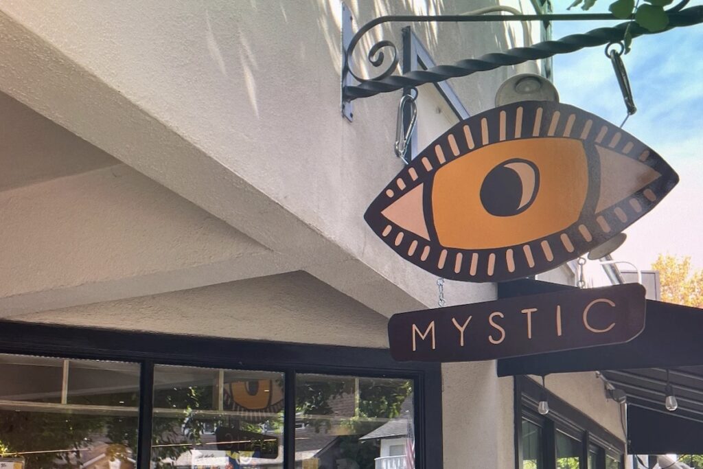 Hanging sign of artistically rendered eye and sign below saying "MYSTIC"