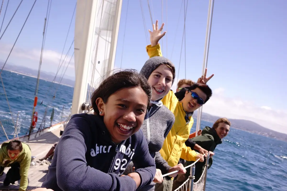 Kids smile on a sailboat for Call of the Sea's outdoor science and sports summer camp in Marin