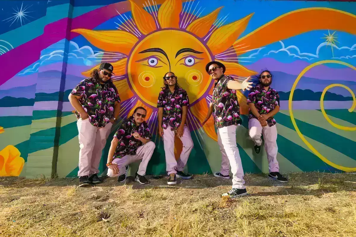 Four men in matching patterned shirts stand in front of a mural: Qiensave, the band coming to marin this June