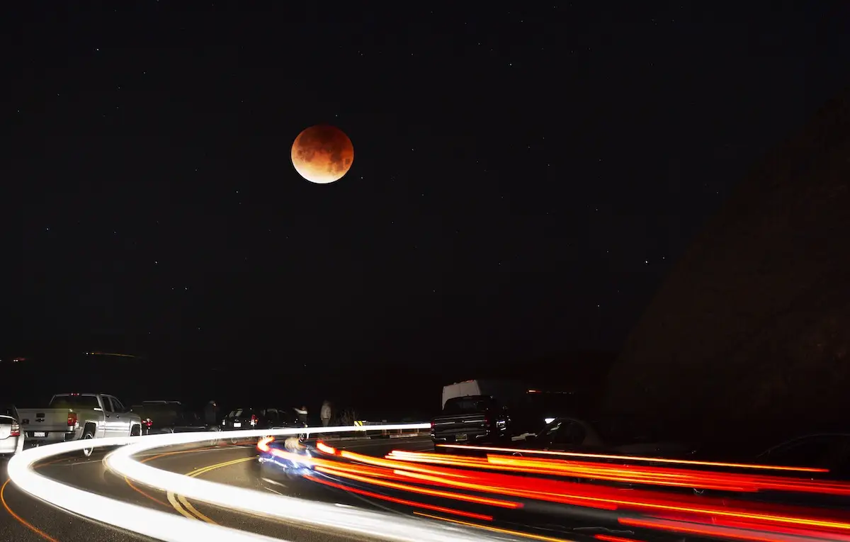 Nature photography of blood moon above long-exposure streaks of car tail lights