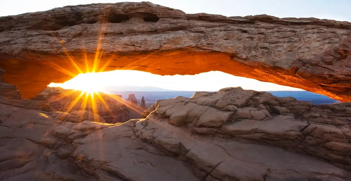 Sun shines through red stone arch at Canyonlands in Utah