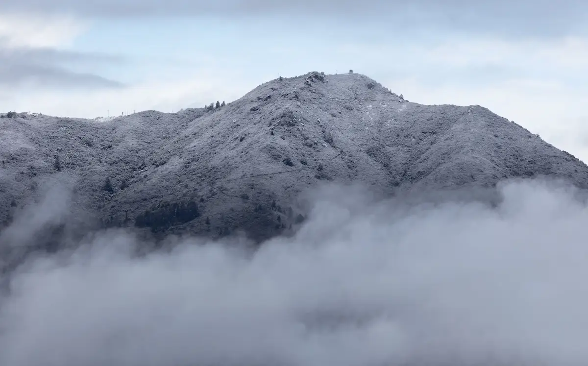 Mount Tamalpais covered in light snow, seen poking out above a cloud