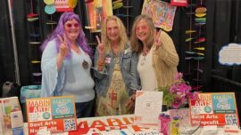 Three women stand behind a colorful booth for Marin Arts.