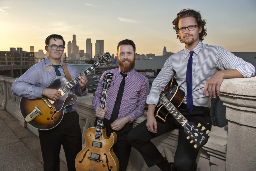 New West Guitars trio posing in front of a city