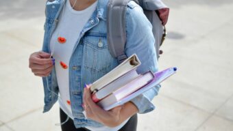 A girl wearing a backpack and holding an armful of textbooks.