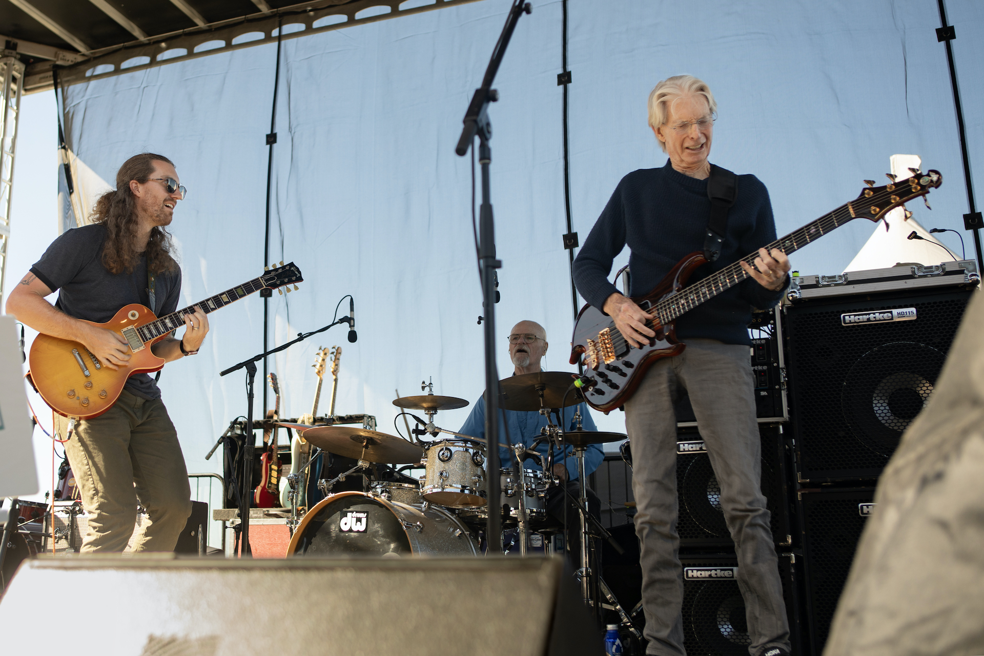 Phil Lesh plays guitar with another guitarist and a drummer on stage.