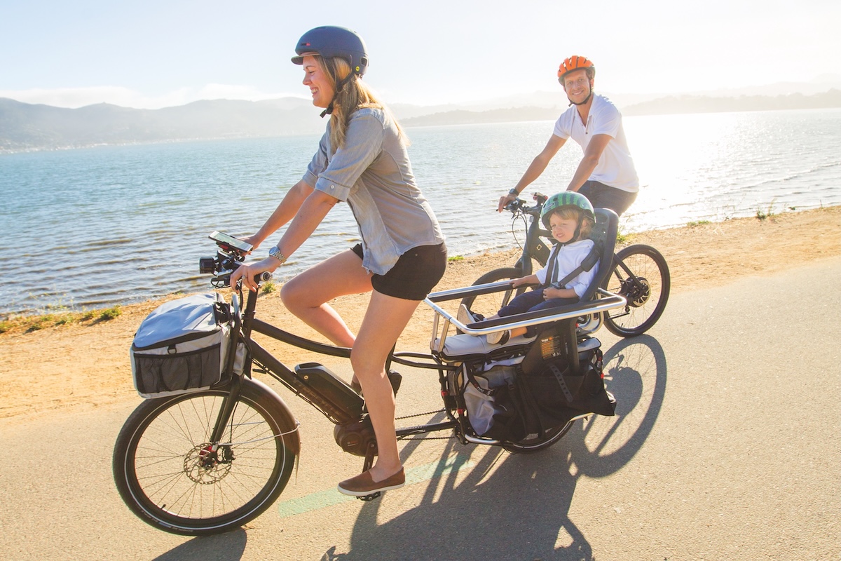 A family rides e-bikes on a road along the edge of water.