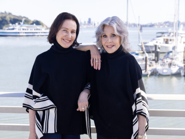 Margaret O'Leary and Jane Fonda wearing their black and white poncho, standing on a pier in Sausalito with the Bay and San Francisco in background.
