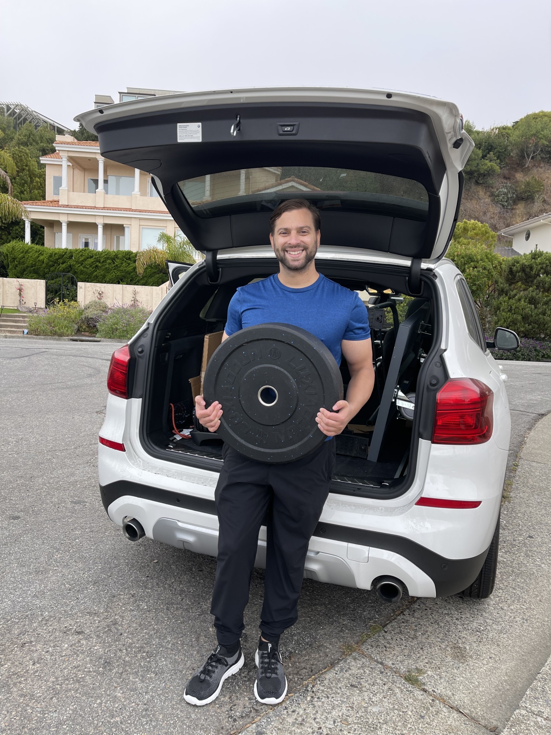Kyle Mastropole stands in front of an open car truck holding weight plates from a gym.