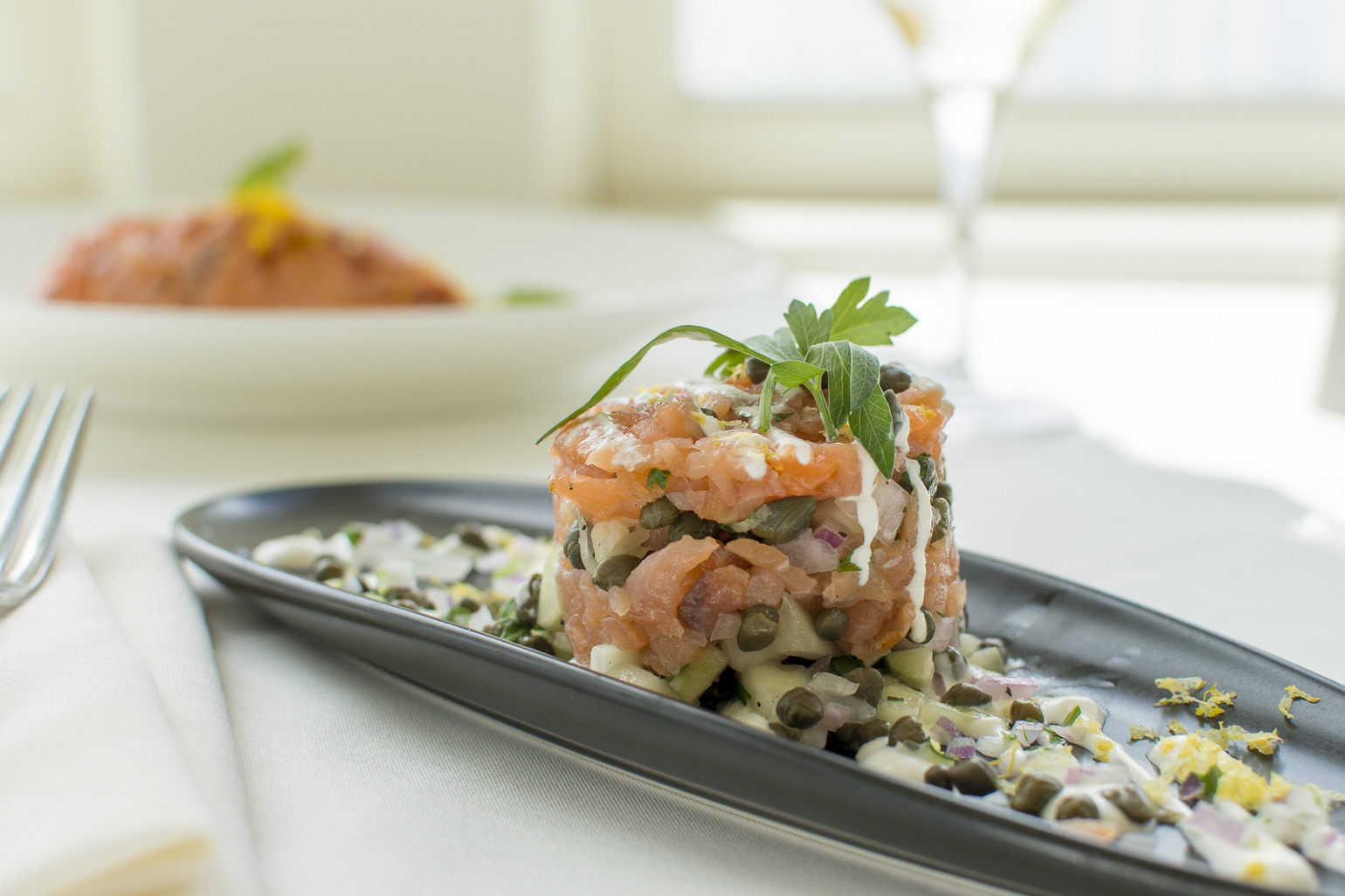 A long black plate with smoked king salmon tartare, garnished with an herb sprig.