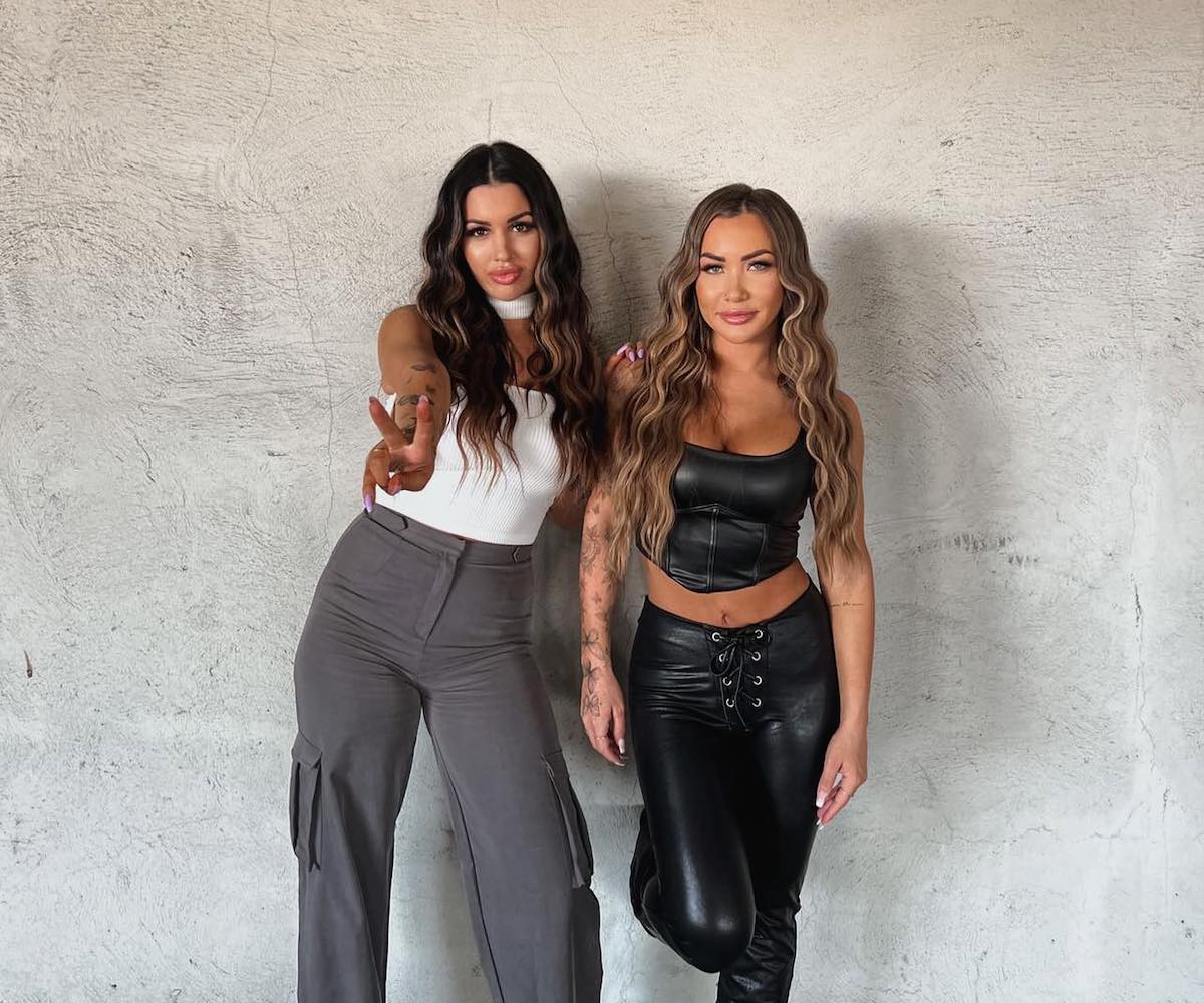 Two women pose with backs against concrete wall for AP Luxe.