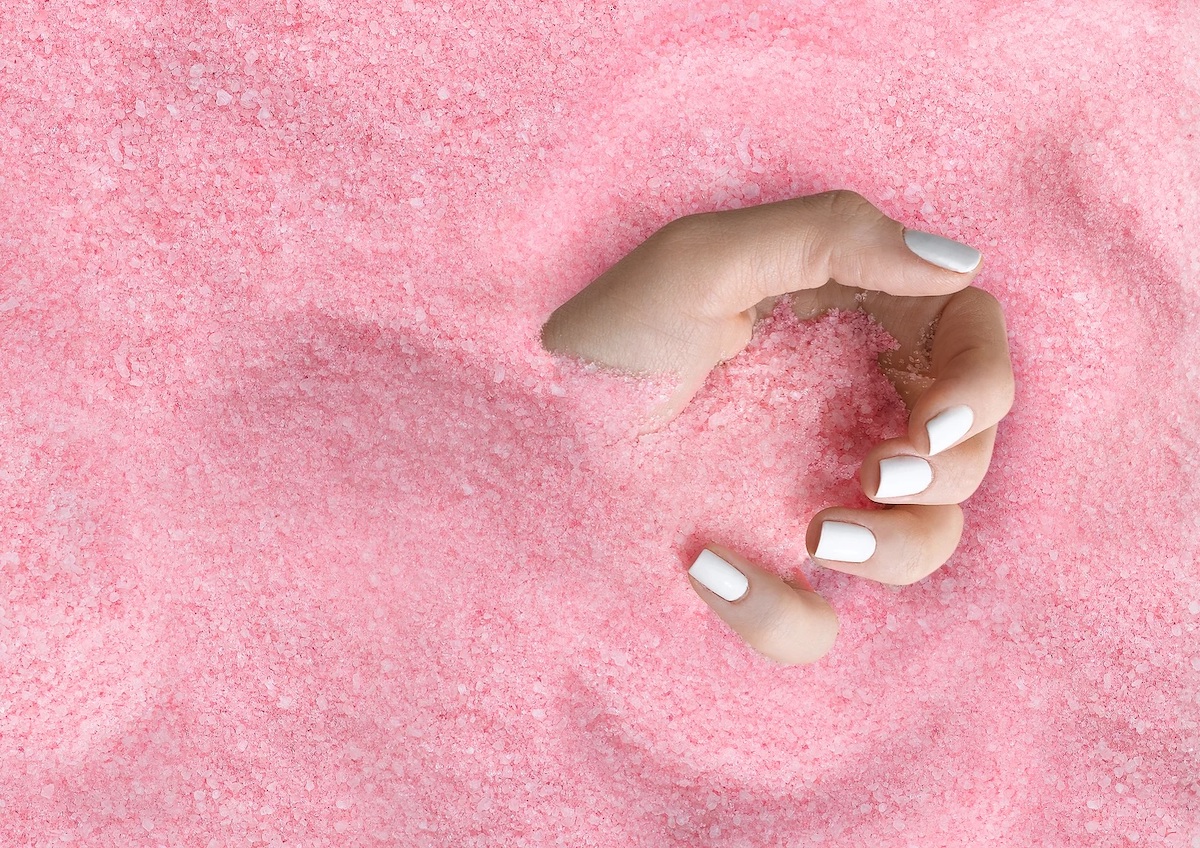 A hand with manicured white nails reaches out of pile of pink beads.