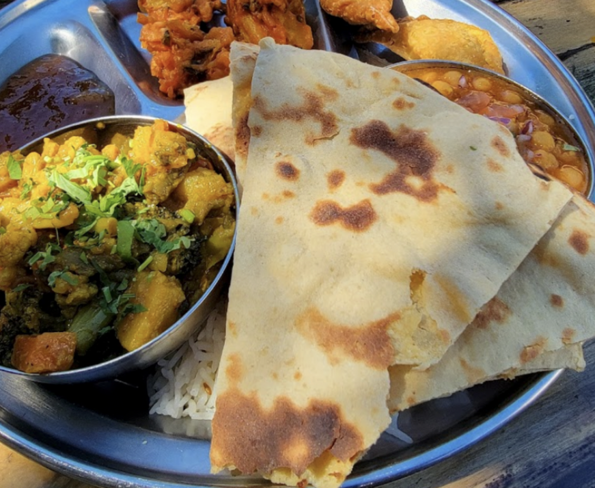 Naan, a bowl with yellow marinated meat and some other sides sit on a plate.