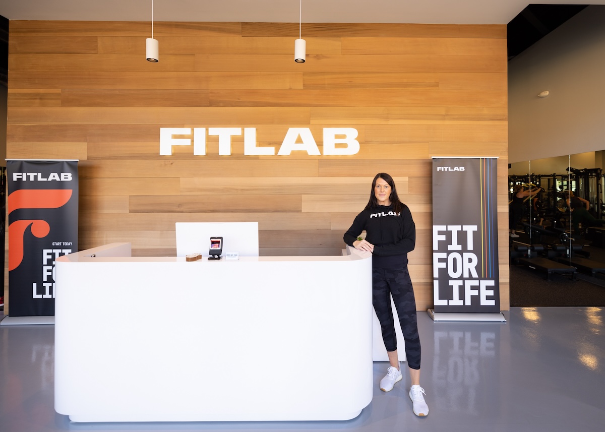 Woman standing to the right of a large desk in the entryway of FITLAB under a sign that reads FITLAB.