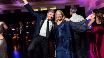 A woman wearing a dark blue long dress with a man wearing a suit and black tie.