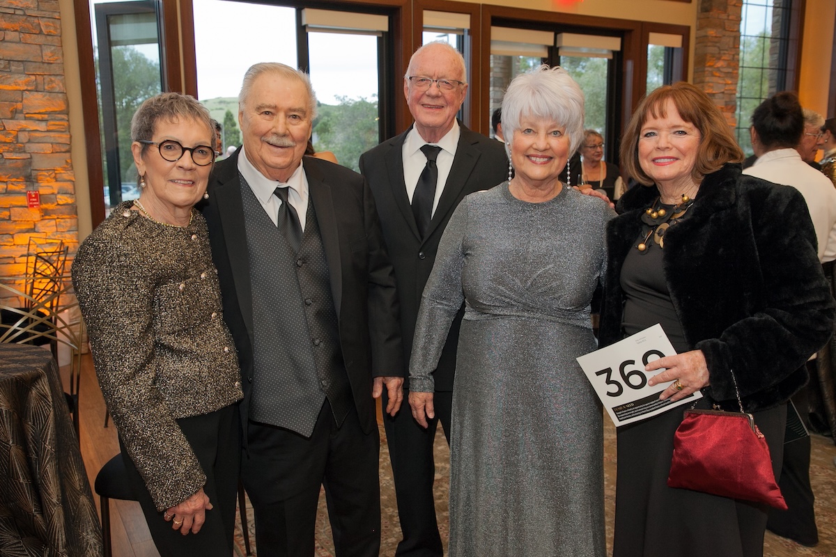 A group of three women wearing nice dresses or pantsuits, and two men wearing ties.