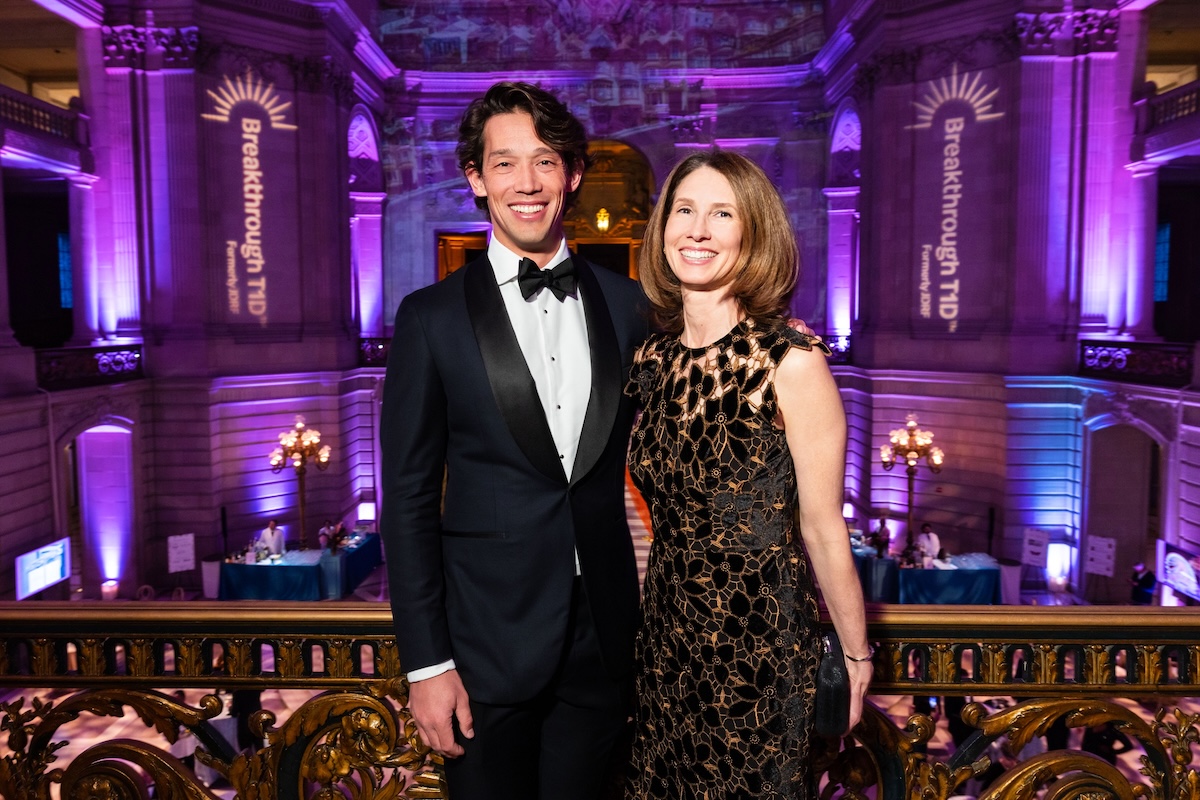 A woman wearing a black lacey dress stands with a man wearing a tuxedo.