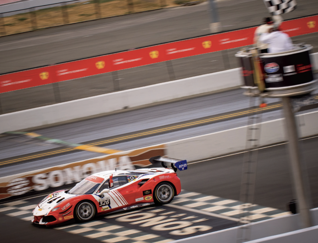 A red and white racecar crosses the finish line of a racetrack.