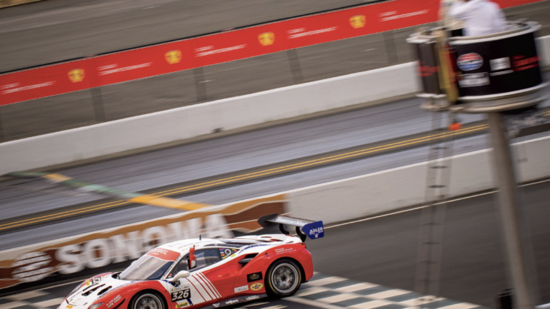 A red and white racecar crosses the finish line of a racetrack.