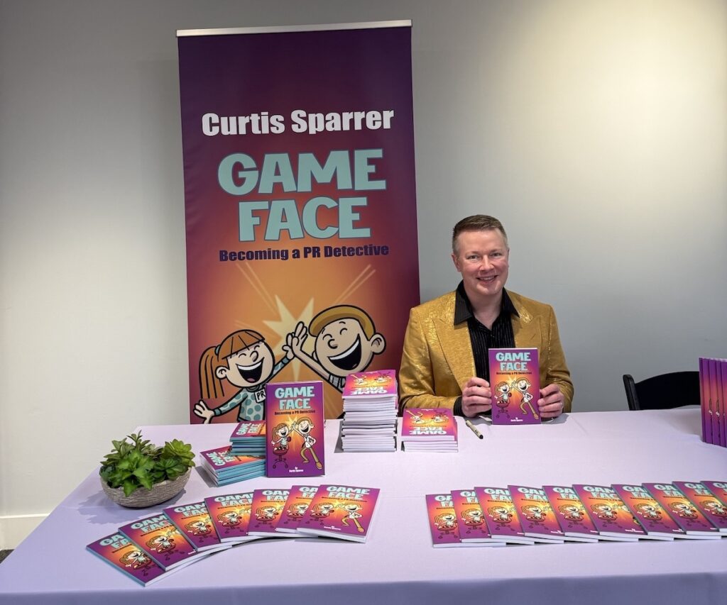 Curtis Sparrer sits at table with copies of his book Game Face