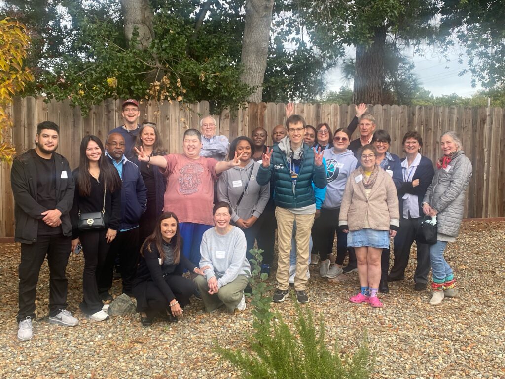 A large group of people standing outside against a wooden fence in a backyard.