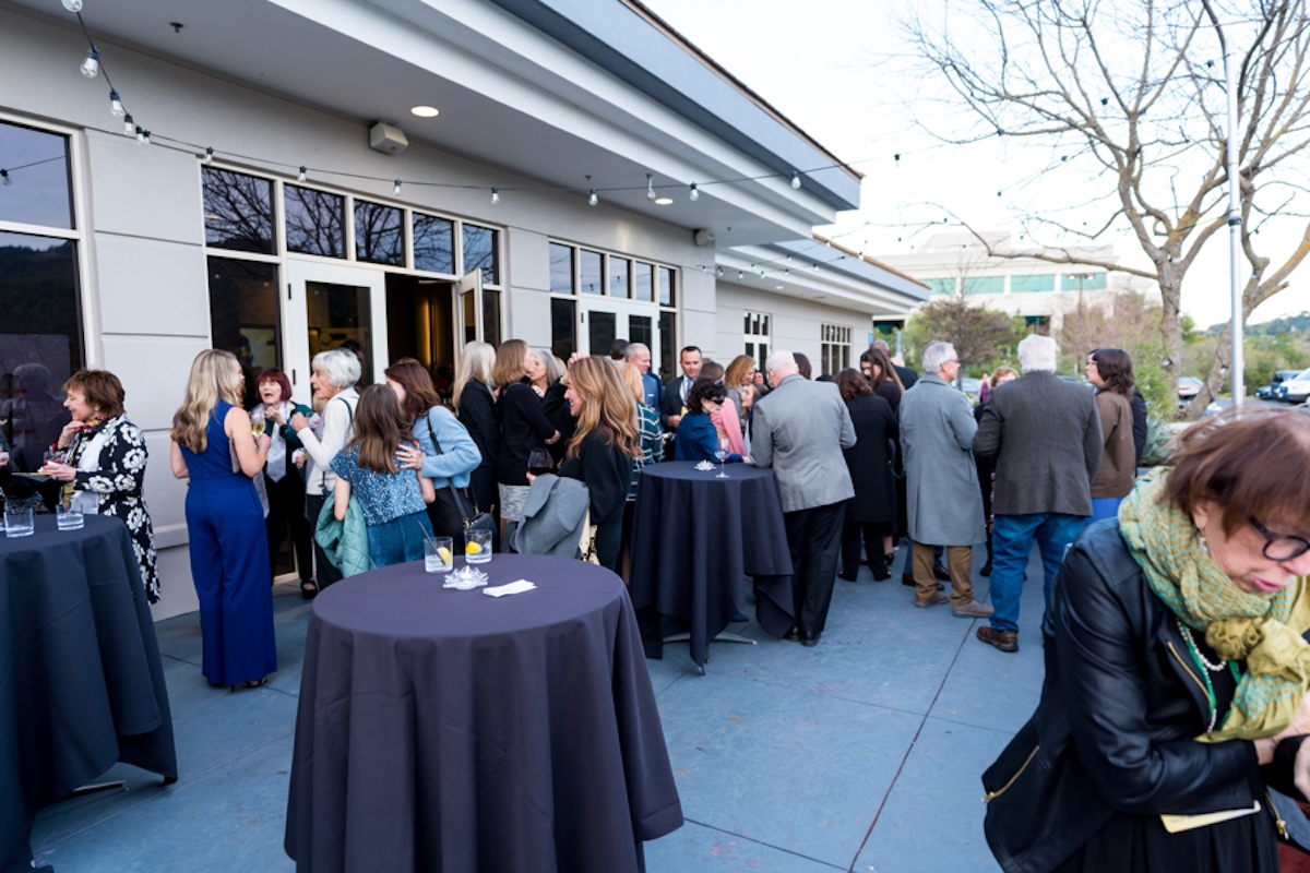 Guests mill around on an outdoor patio with cocktail tables around.