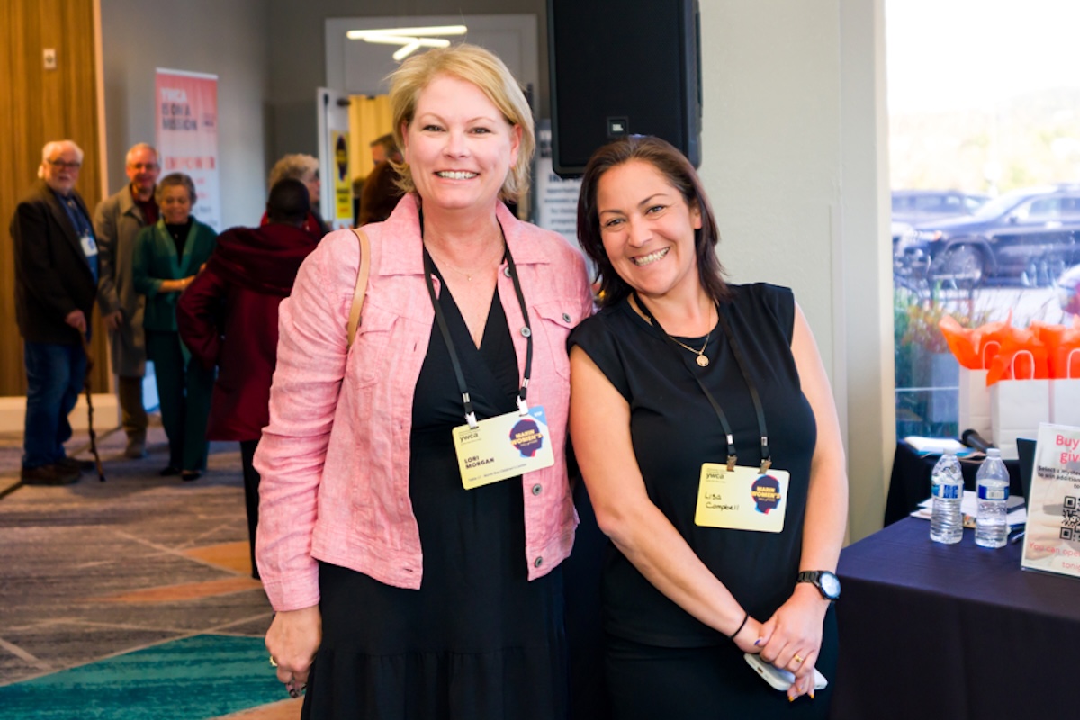 Two women wearing black dresses, one wearing a pink jacket too, and also yellow badges.