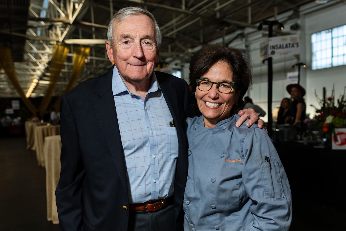 A man wearing a button down and black cardigan and a woman in a chef's uniform.