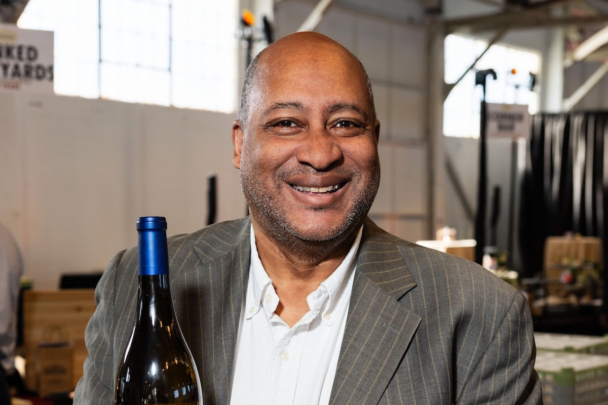 A man in a striped suit holds a bottle of wine.