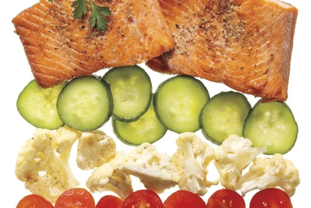 A layered pattern with salmon, cucumber, cauliflower and tomatoes all stacked on top of each other.