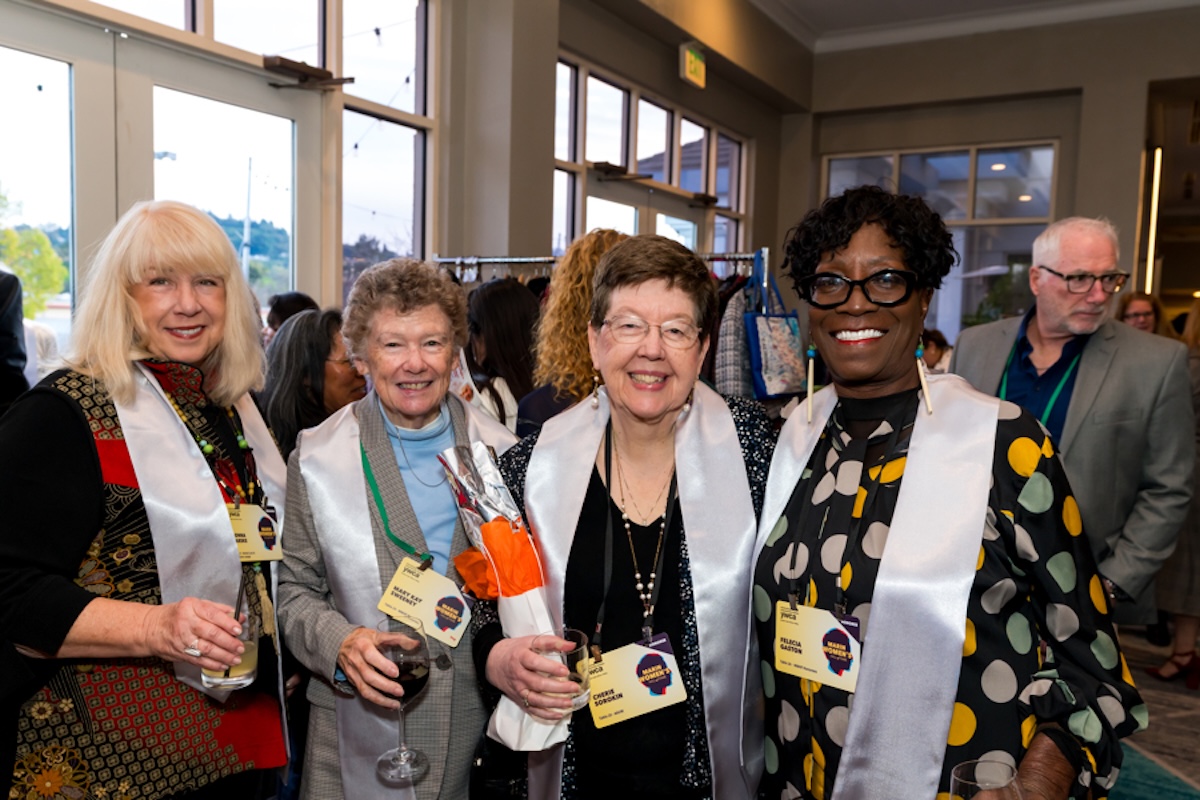 A group of four women holding drinks and wearing yellow badges.