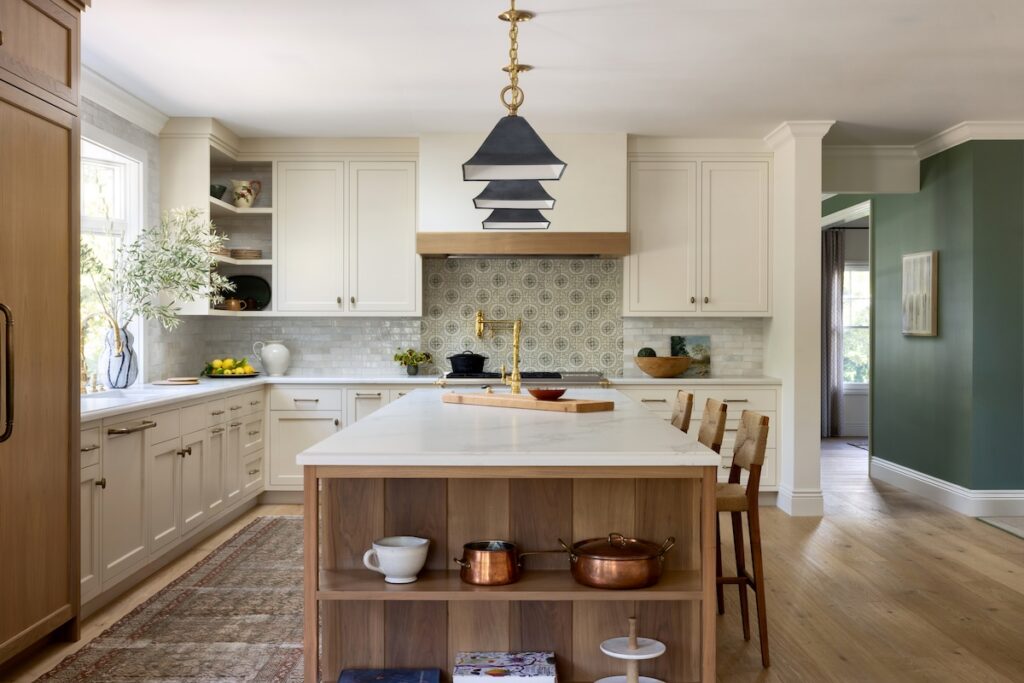 Warm and elegant kitchen featuring a large white oak island with Caesarstone countertops, a patterned tile backsplash, brass fixtures, and vintage-inspired lighting, designed by Caitlin Jones Ghajar.