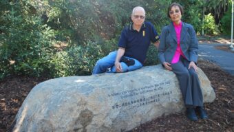 Dr. Jean Chan and a man sit on a long rock engraved with writing and characters.