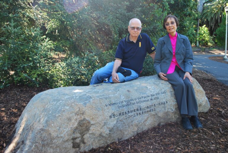 Dr. Jean Chan and a man sit on a long rock engraved with writing and characters.