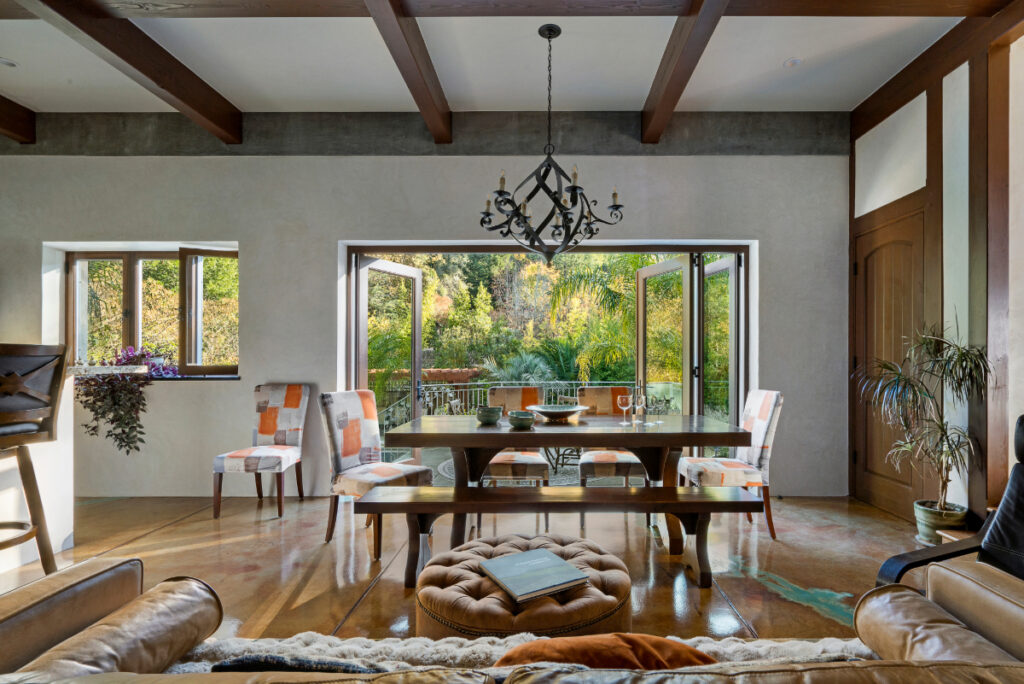 The ADU’s dining room with a large wooden table and colorful chairs, opening to a lush backyard garden through wide bi-fold doors.