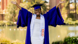 A new graduate student standing with her arms spread out smiling.