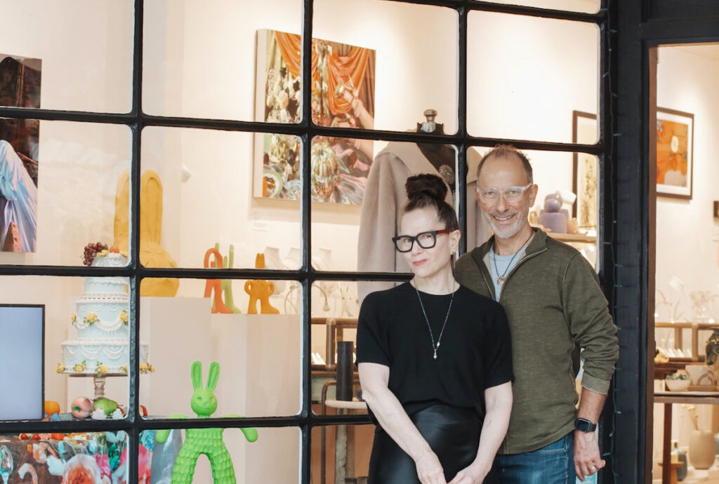 A man and a woman standing outside of an art store window smiling.