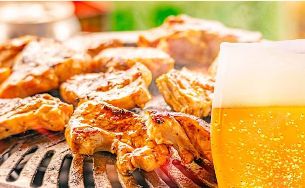 A plate with meat roasting on a grill and a beer.