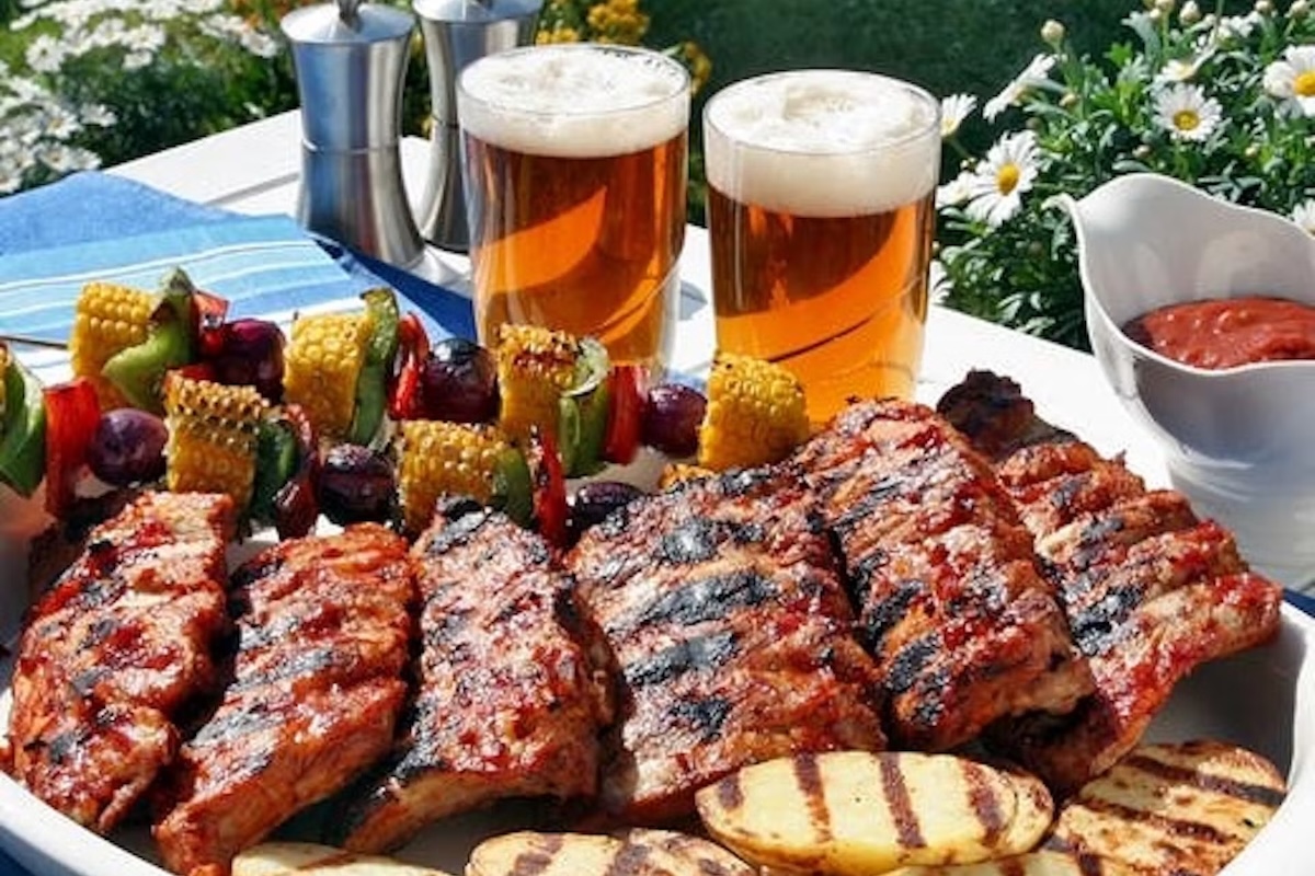 A plate full of sliced grilled steak and chicken, kebabs, two beers and ketchup.