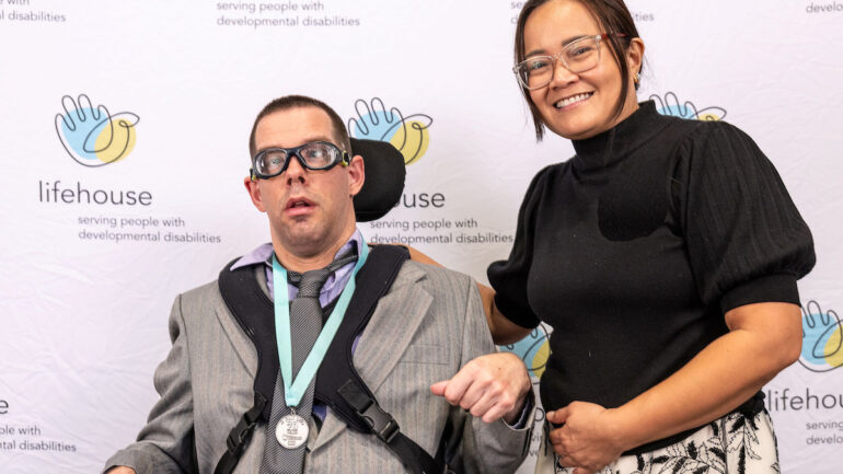 A woman patting a man with a disability on the back and smiling.
