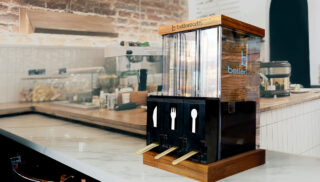 A dispenser holding stacked wooden forks, knives, and spoons stands
