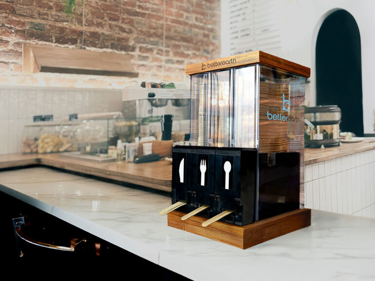 A dispenser holding stacked wooden forks, knives, and spoons stands