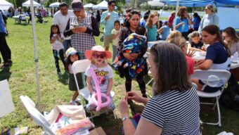 A woman making a little girl a balloon animal at a gathering