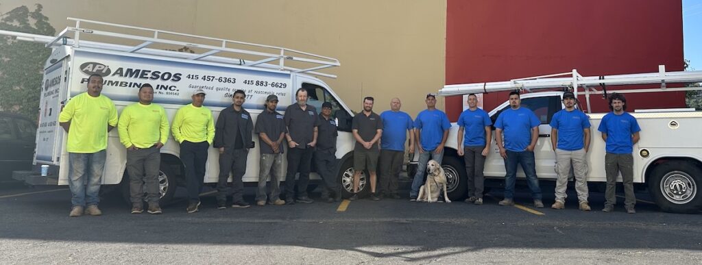 A team of employees stand outside in front of some work trucks.
